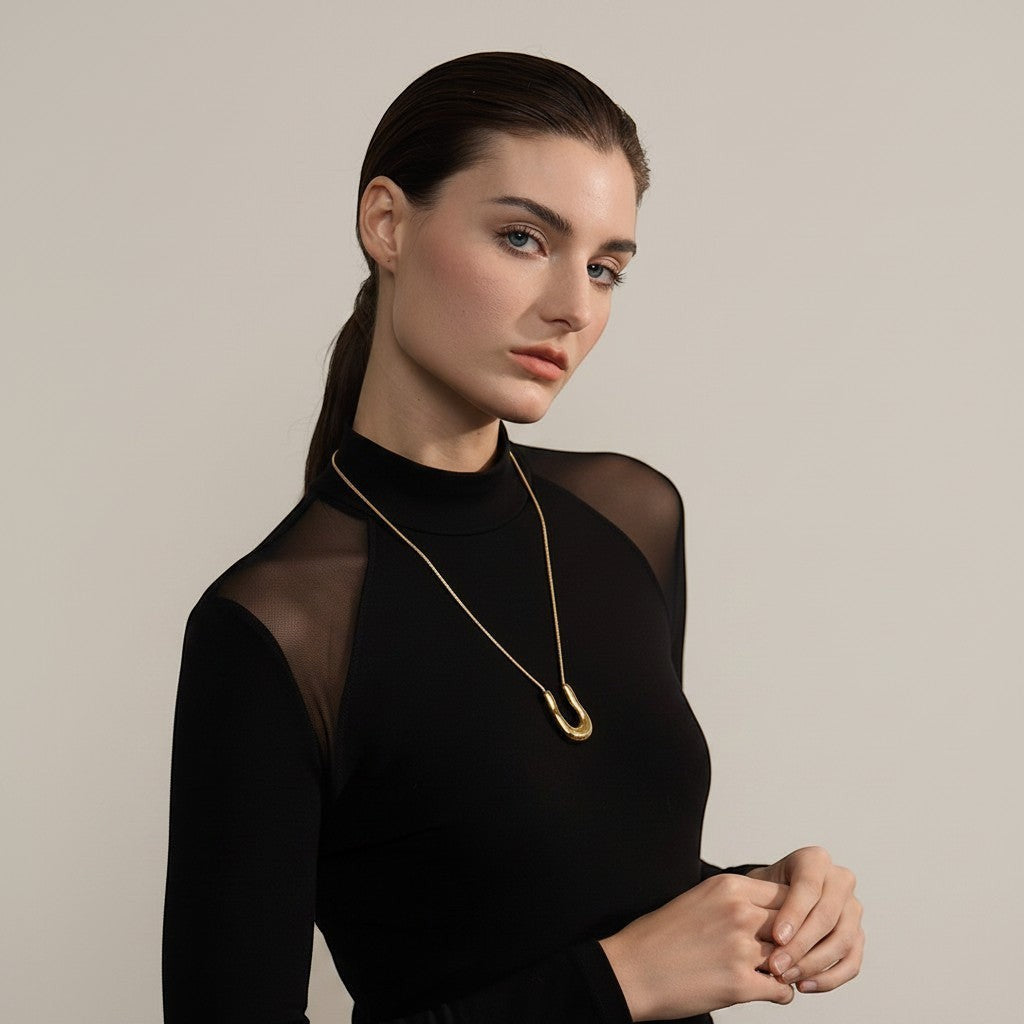 PRO RAY ELORA gold sculptural pendant necklace with organic curves on a fine chain. Model wears black mesh top.